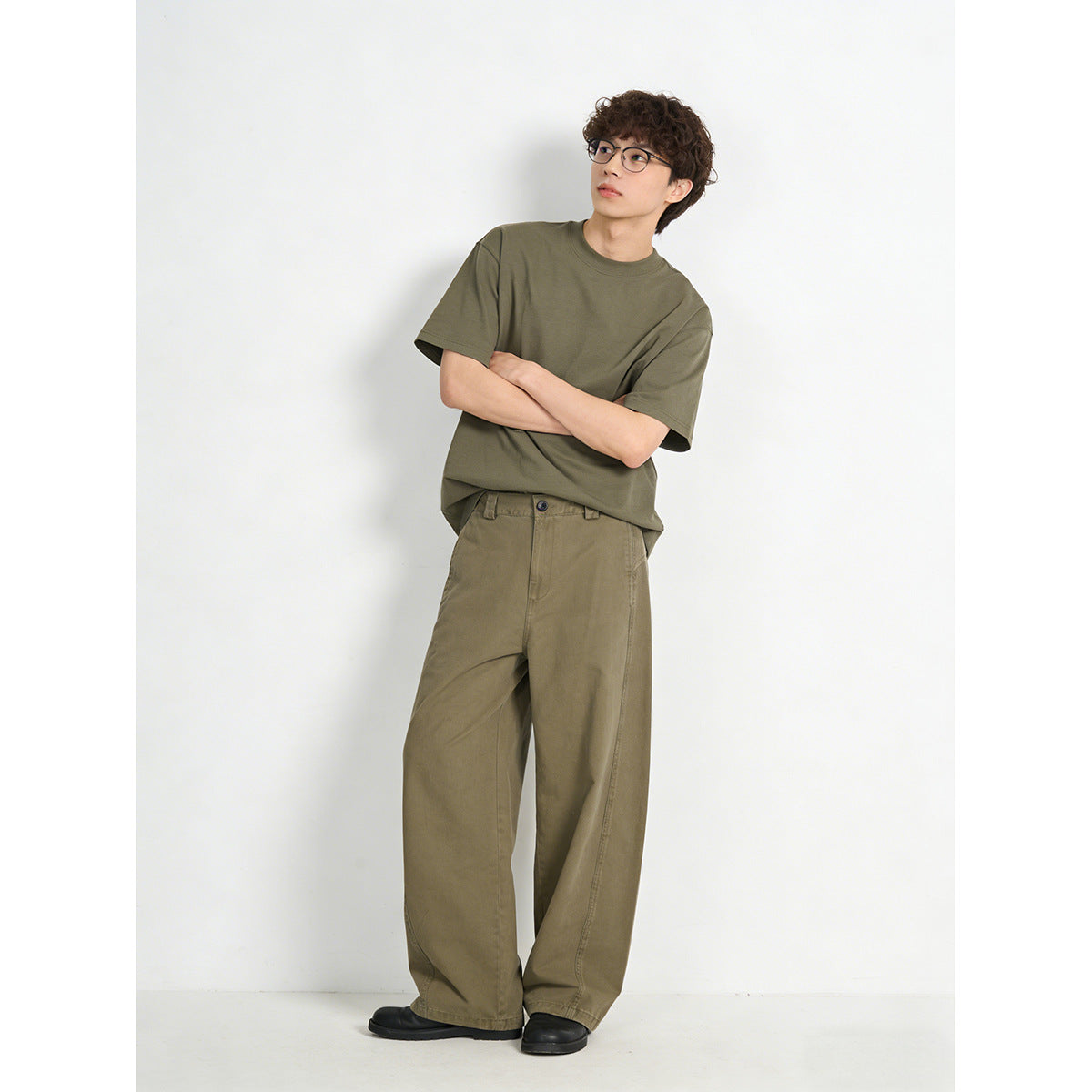 Model wearing a muted olive short-sleeve crewneck T-shirt and loose taupe wide-leg trousers, shown full length.