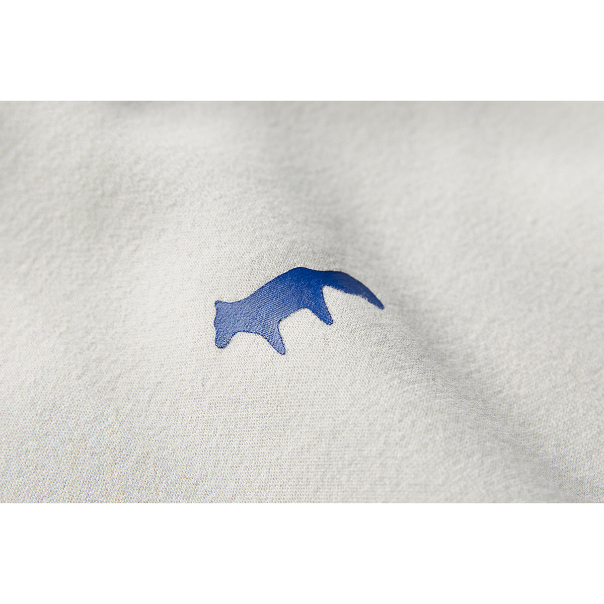 Close-up of a small blue animal-shaped emblem embroidered on off-white sweatshirt fabric.