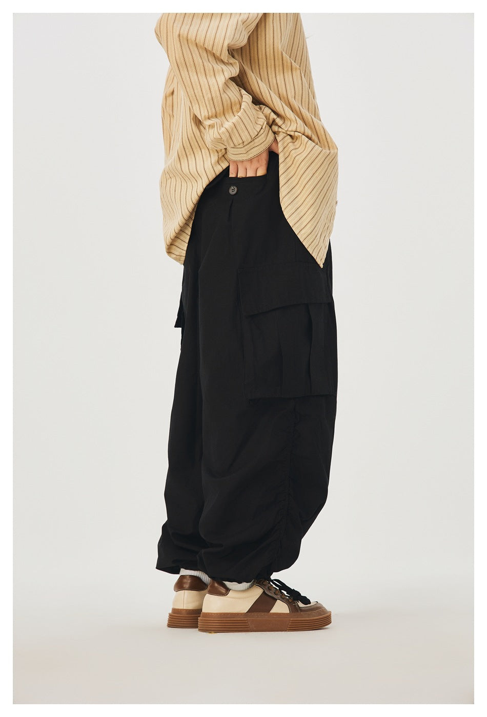 Side view of a model wearing loose black cargo pants with a large flap pocket and gathered hems.