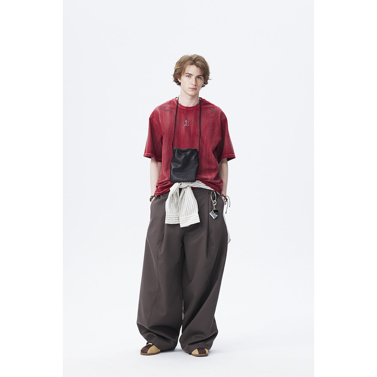 Model wearing a faded red graphic T-shirt with loose dark trousers and a striped shirt tied at the waist.
