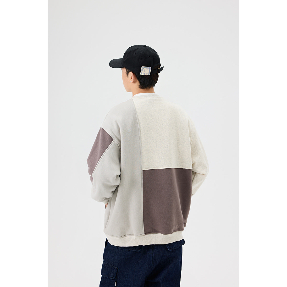 Back view of a model wearing a cream, light gray, and taupe color-block crewneck sweatshirt.