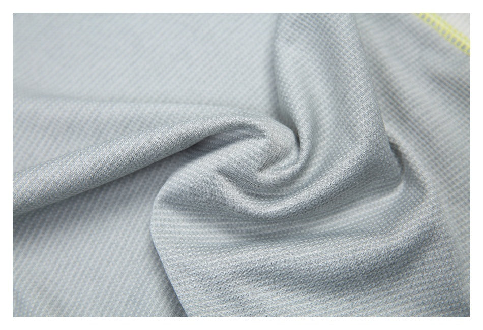 Close-up of light gray textured shirt fabric gathered into folds, with a small section of neon-yellow stitching visible.