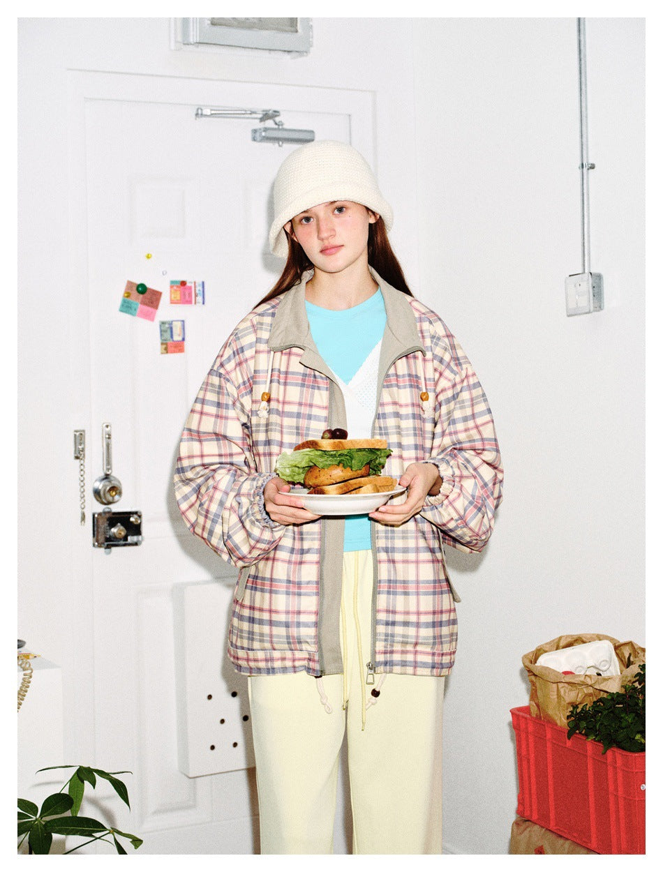 Closer front view of a model wearing a pastel plaid jacket with gray trim over a turquoise top and cream pants.