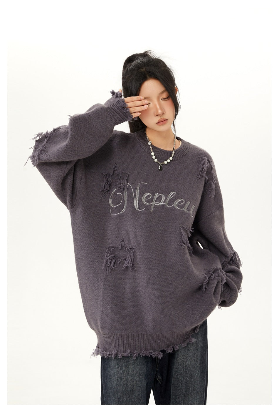 Closer view of a model wearing an oversized charcoal-gray sweater with script lettering and distressed patches.