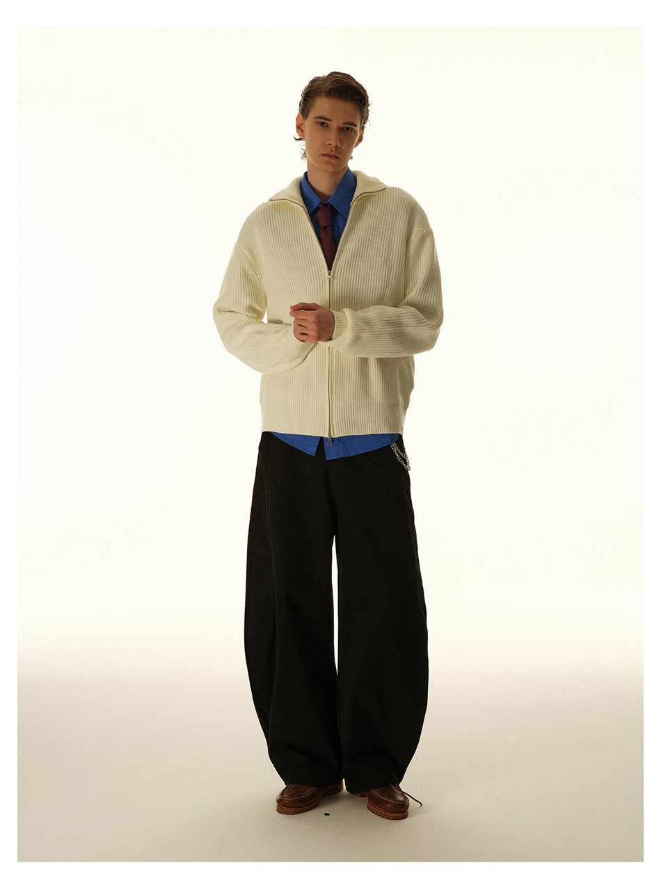 Front view of a model wearing a cream ribbed zip-up cardigan over a blue shirt and tie with wide black trousers.