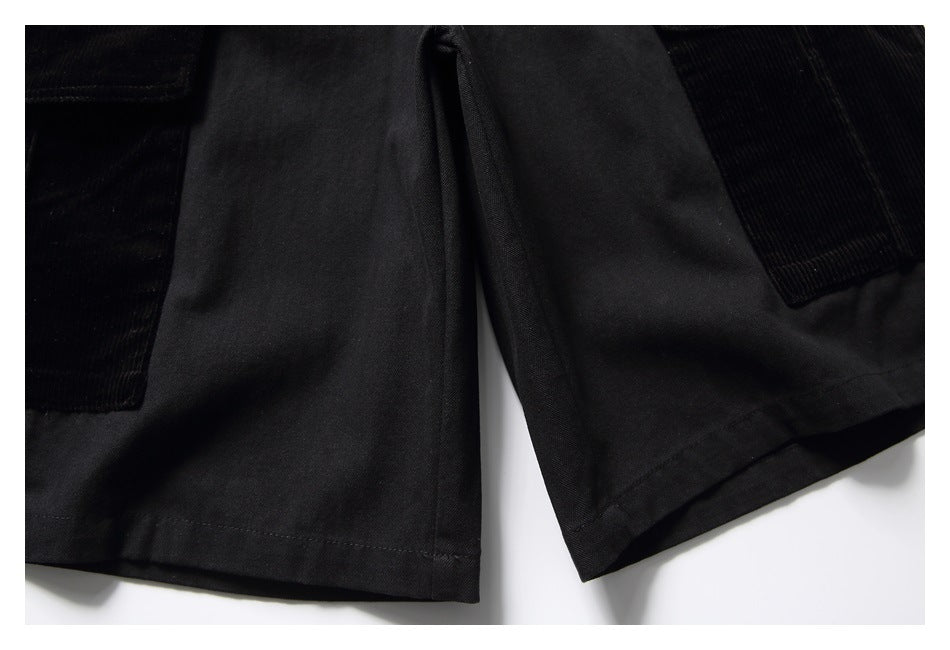 Cropped view of the lower front of black shorts with large side pockets and stitched hems.