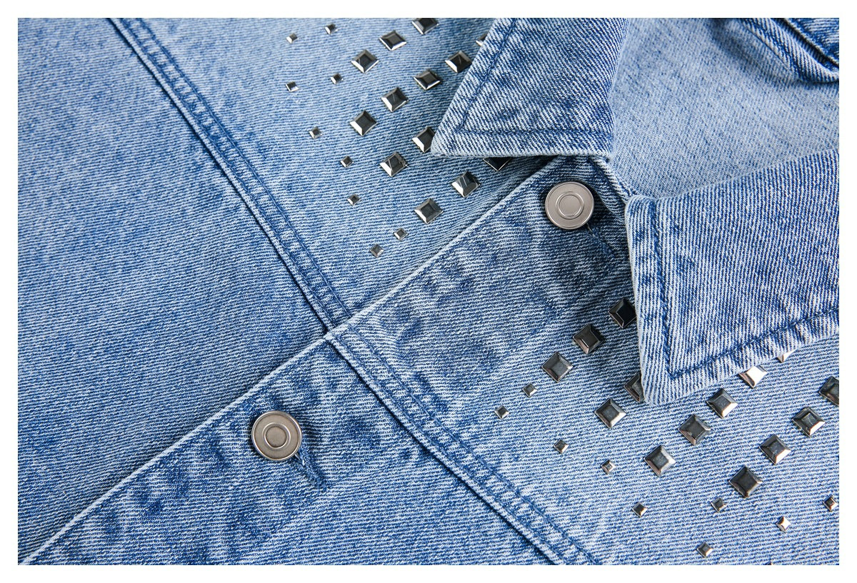 Close-up of a light blue denim jacket front with a pointed collar, silver-tone buttons and dark square studs.