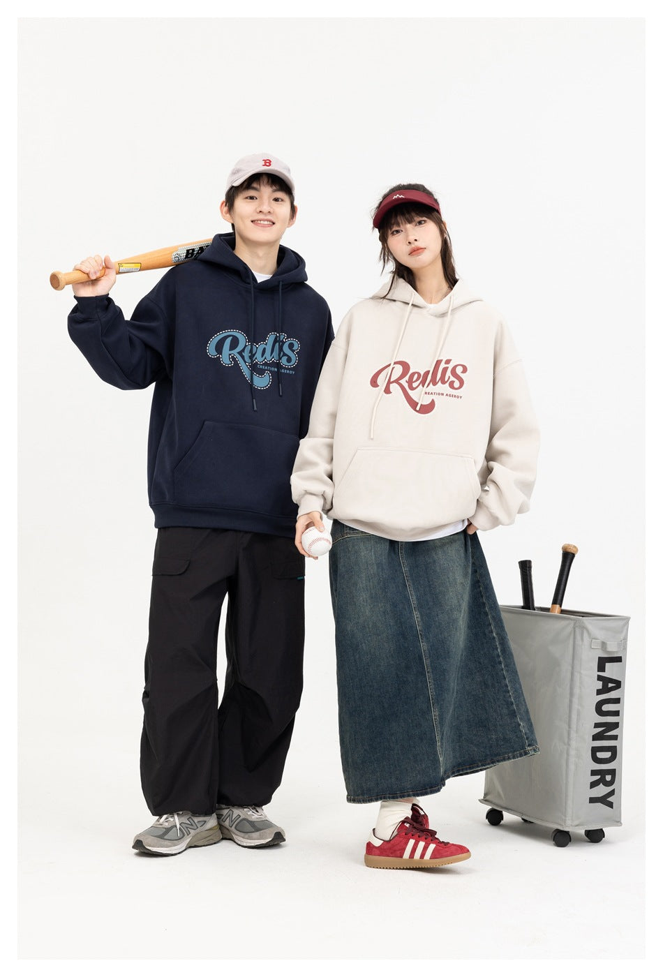 Two models show navy and cream graphic hoodies with a baseball bat and ball beside a laundry cart.