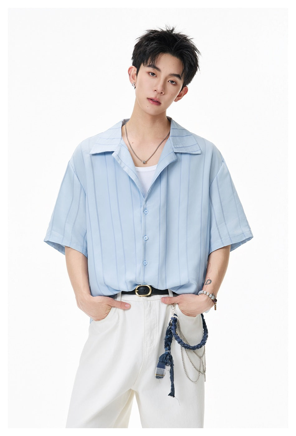 Model in light blue striped short-sleeve shirt with open collar over white tank, close-up with white pants and chain