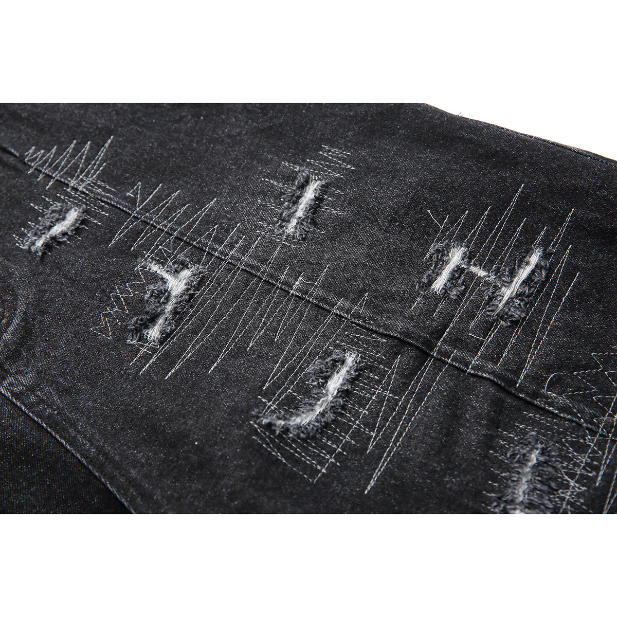 Close-up of black denim shorts with multiple distressed patches and pale decorative stitching.