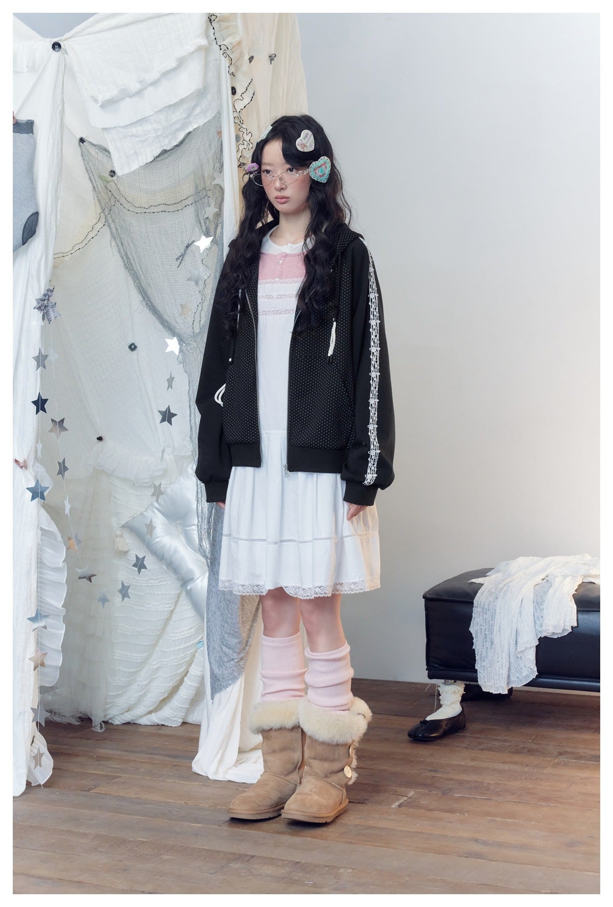 Model in a black dotted hooded jacket with white sleeve graphics, shown over a white dress from a slight angle.
