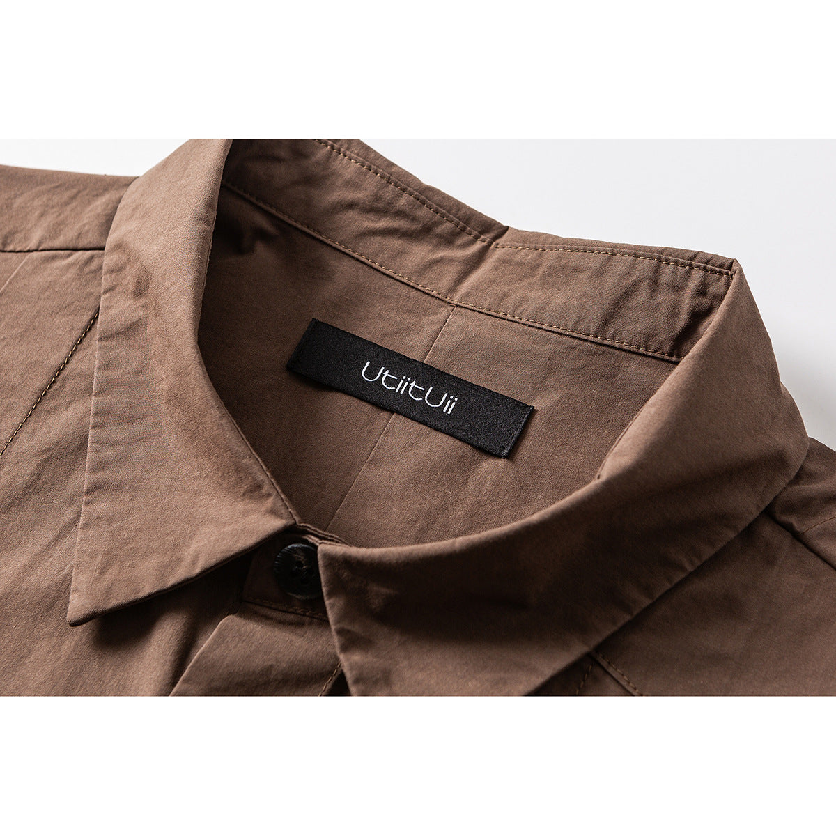 Close-up of a brown shirt collar, button, stitching, and black neck label.