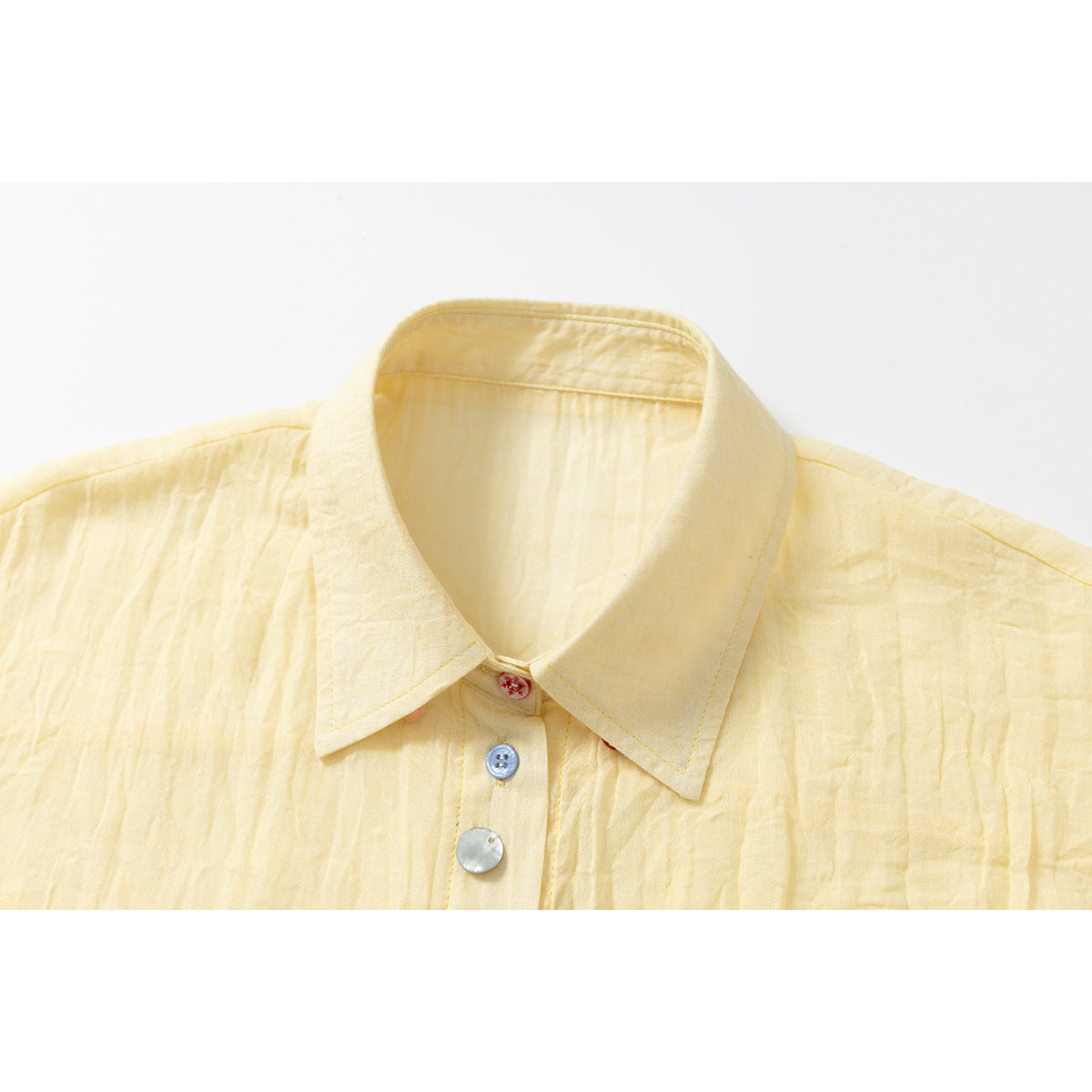 Close-up of a pale yellow shirt collar and placket with contrasting buttons.