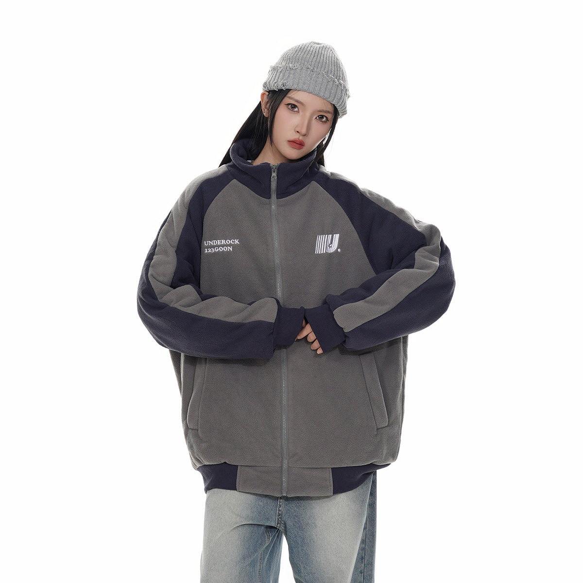 Model wearing a charcoal gray and navy color-block zip-up jacket with a high collar and a gray knit beanie.