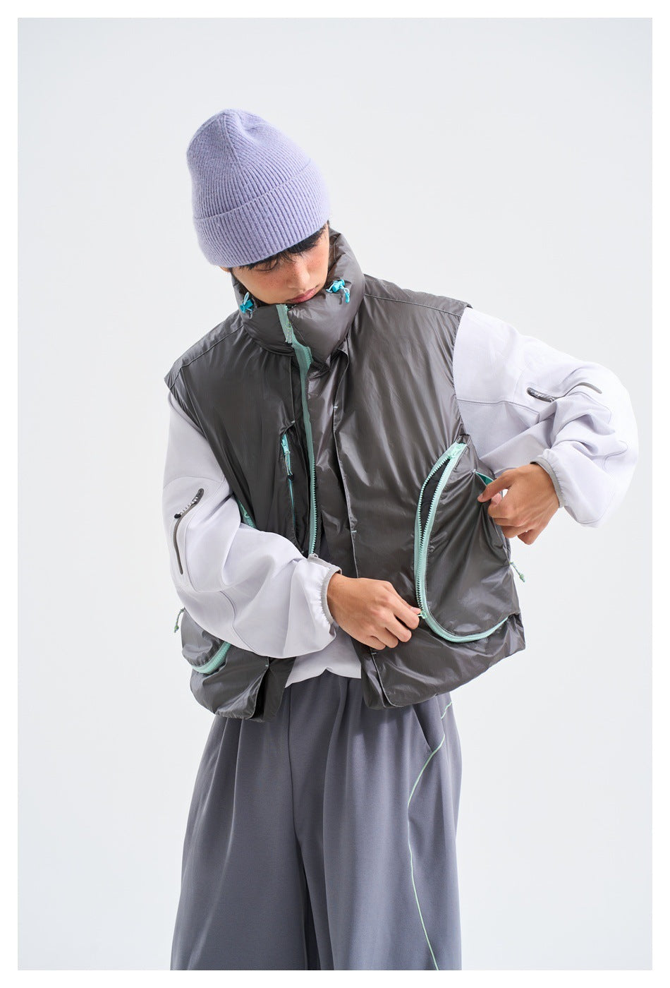 Model in a charcoal-gray vest with turquoise-trimmed pockets, opening a pocket over a white top.
