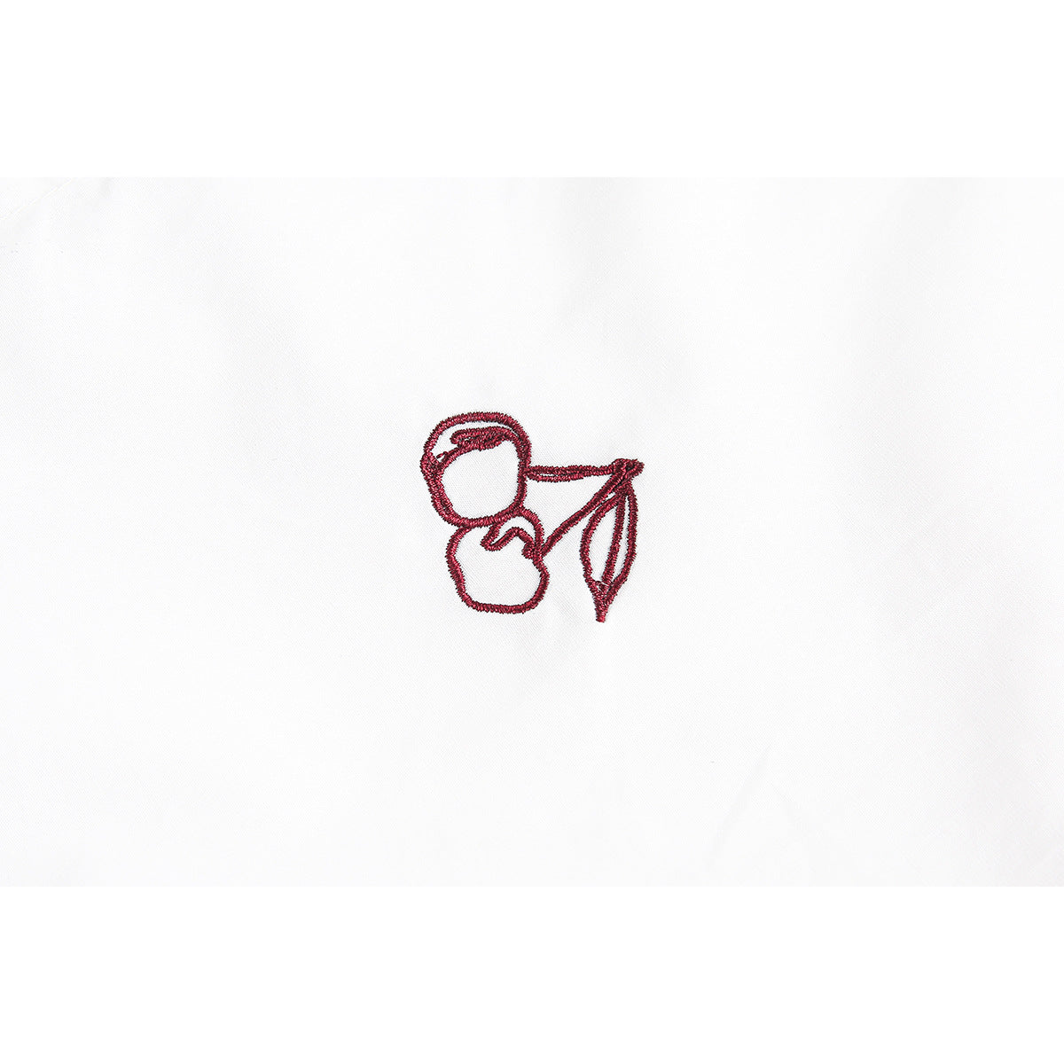 Close-up of a small red embroidered cherry motif on white shirt fabric.