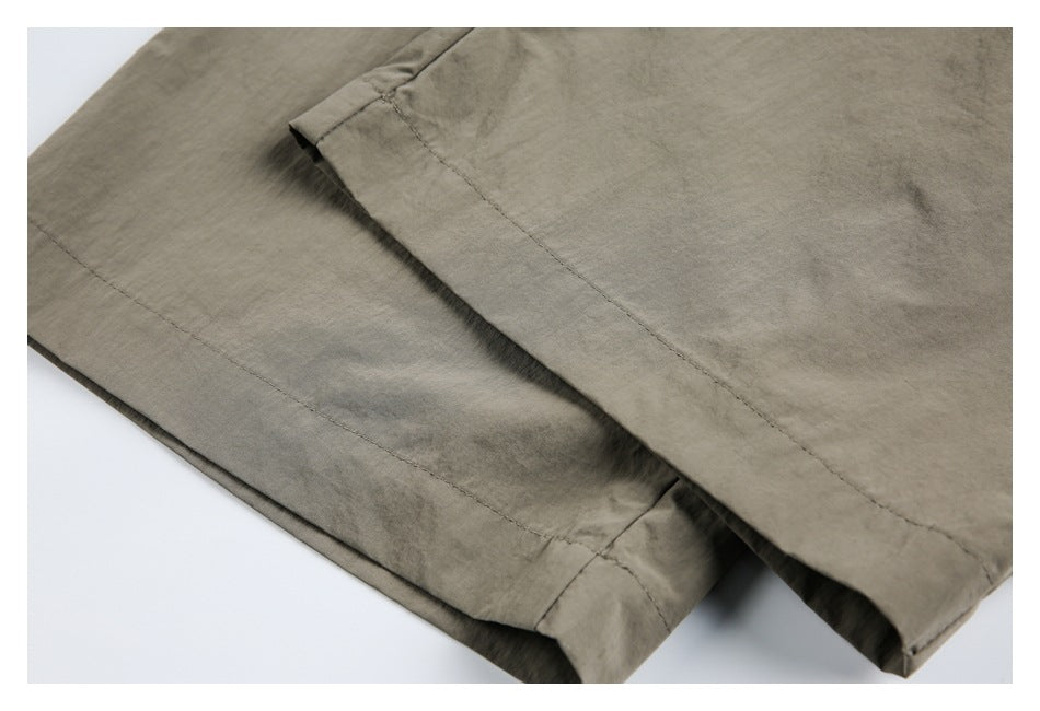 Close-up of olive-gray trousers showing a stitched hem and overlapping fabric panels.