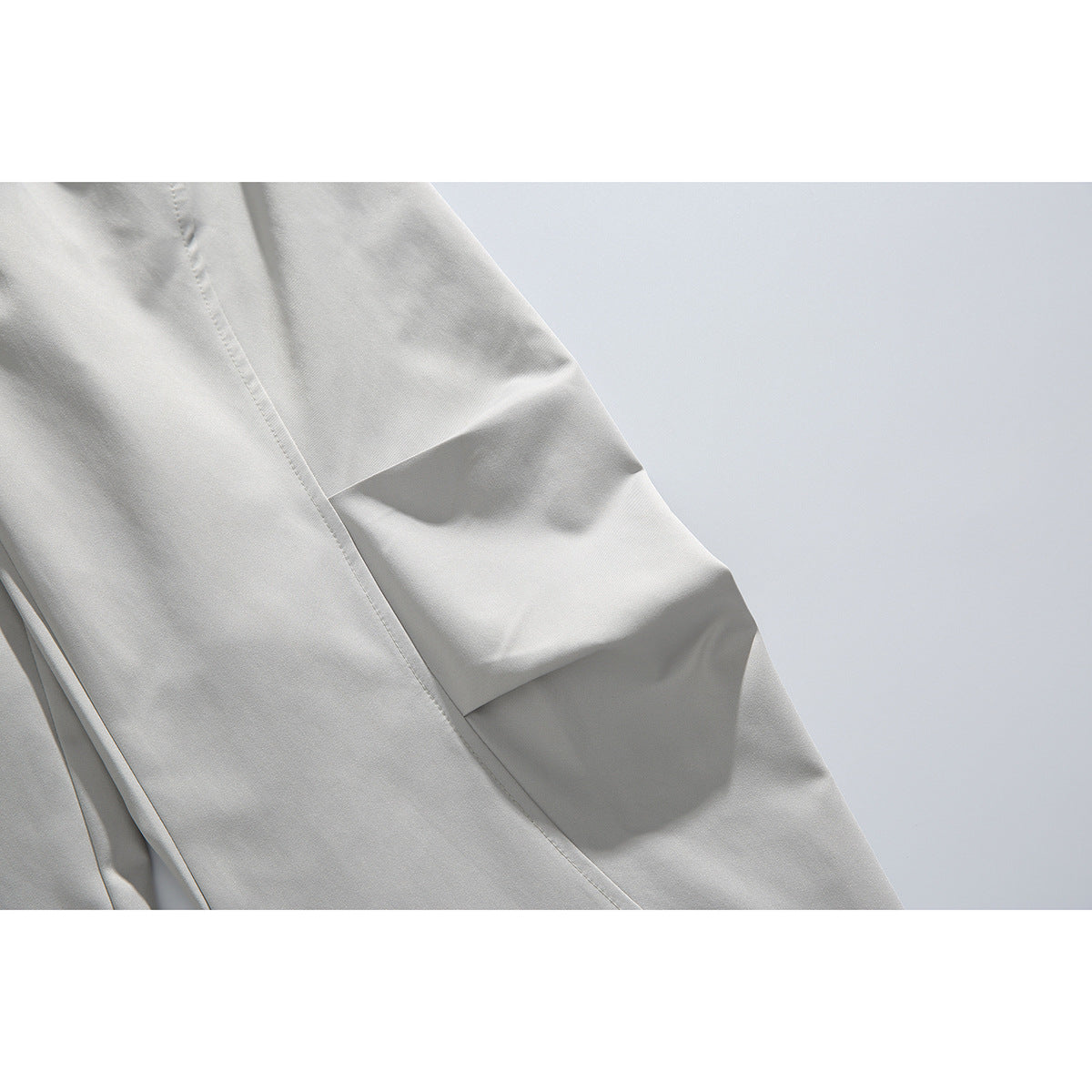 Close-up of light gray trouser leg with a stitched seam and folded knee detail.
