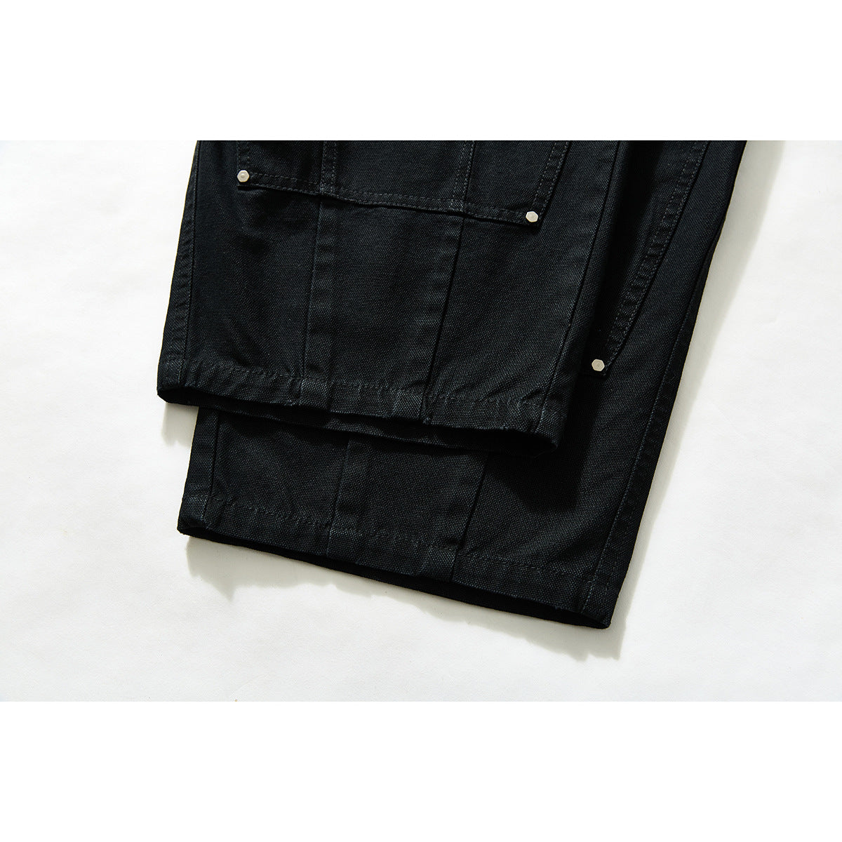 Close-up of black pants legs with stitched utility panels, metal rivets and straight hems.
