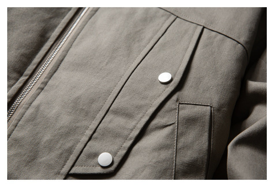 Close-up of a taupe jacket with a metal zipper, snap-button storm flap, and vertical pocket.