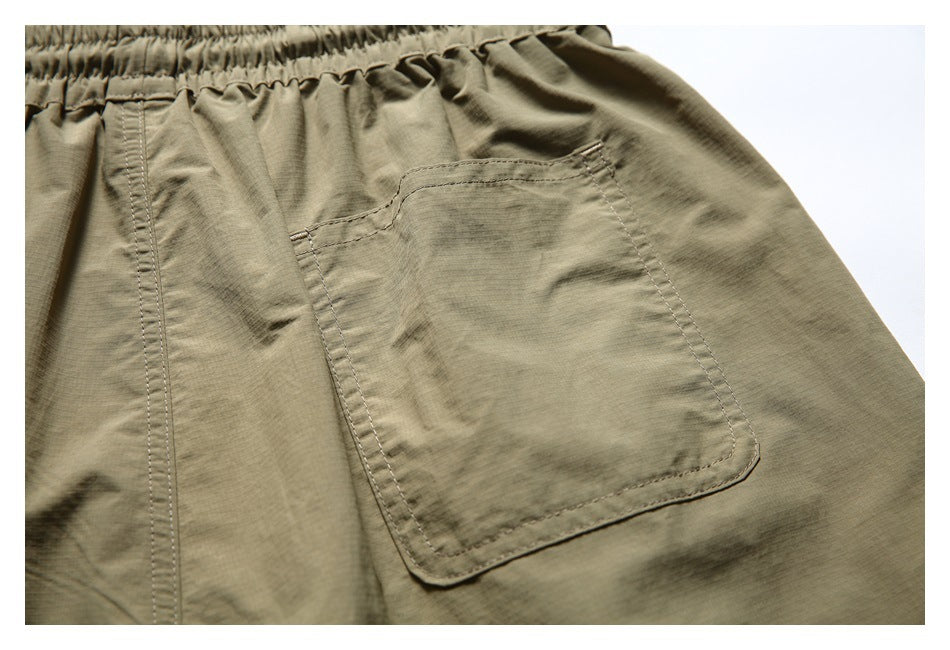 Close-up of a stitched patch pocket on the rear of olive-khaki shorts.