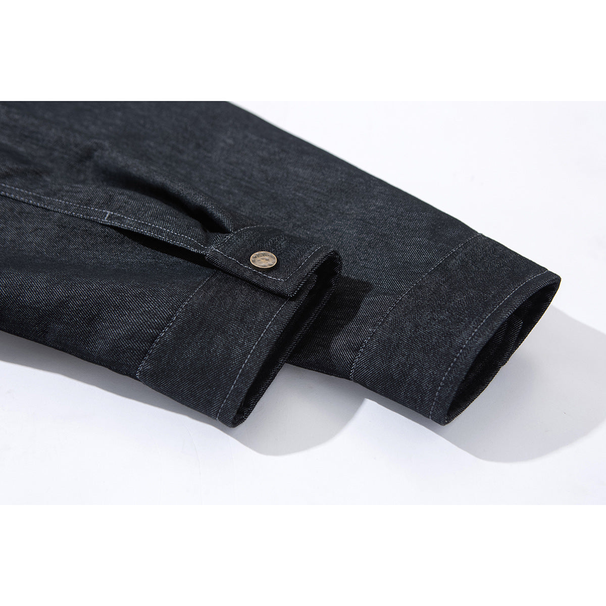 Close-up of a dark indigo jacket sleeve cuff with a buttoned tab and stitched seams.