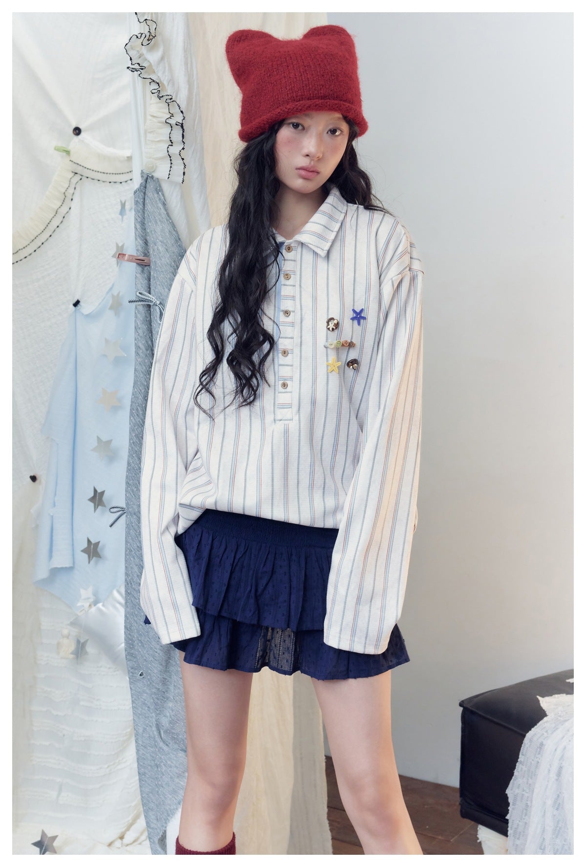Model wearing an oversized white shirt with thin blue and red stripes and colorful chest embellishments, with a navy tiered