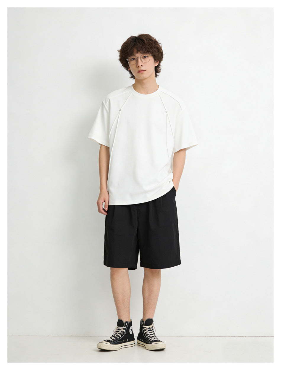 Front view of a model in a white short-sleeve crew-neck shirt with shoulder details and loose black shorts.