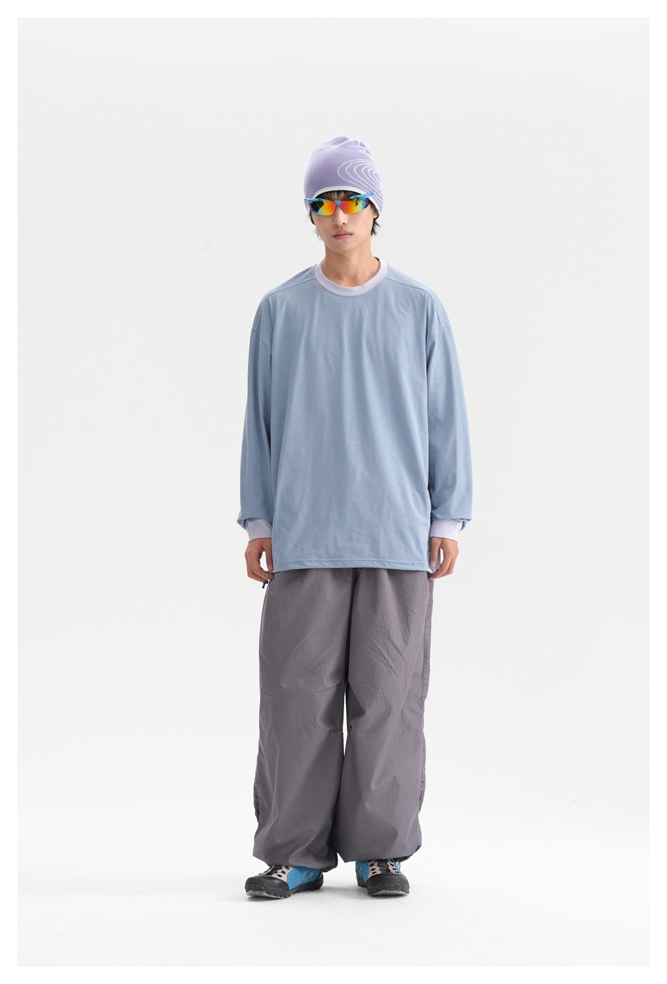 Front view of a model wearing a light-blue long-sleeve top with lavender trim and loose gray trousers.