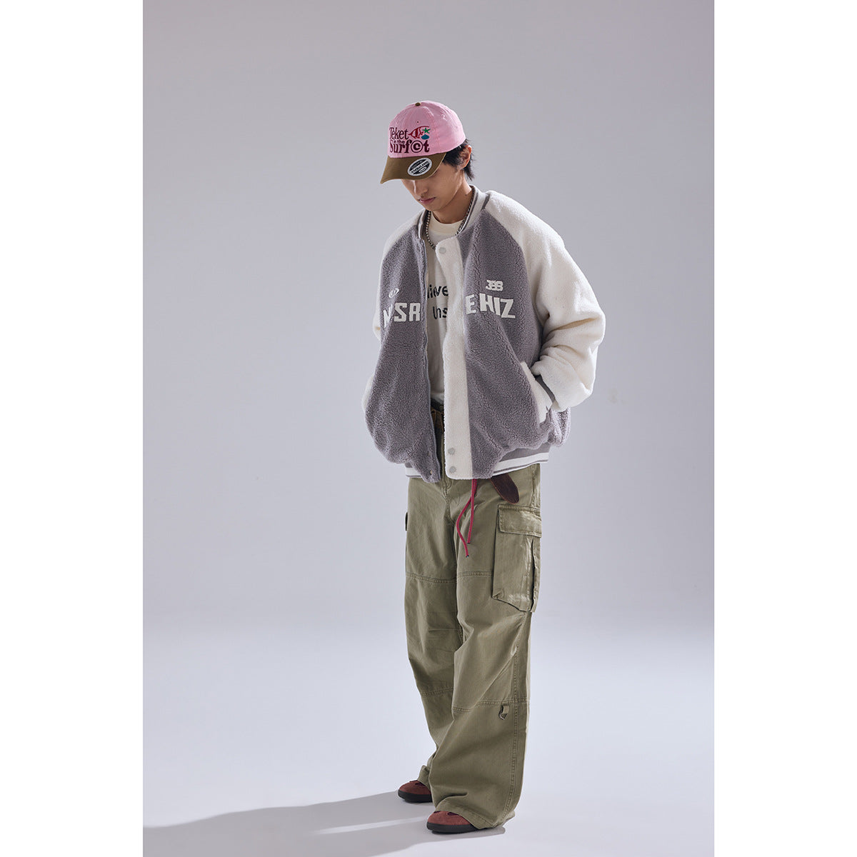 Model wearing a gray-and-white color-block fleece varsity jacket with large chest lettering, shown from the front.