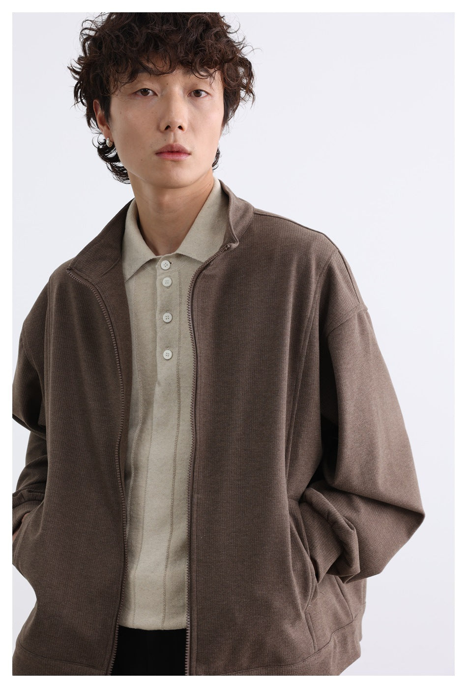 Close view of a model wearing an open brown zip-front jacket over a light beige collared shirt.