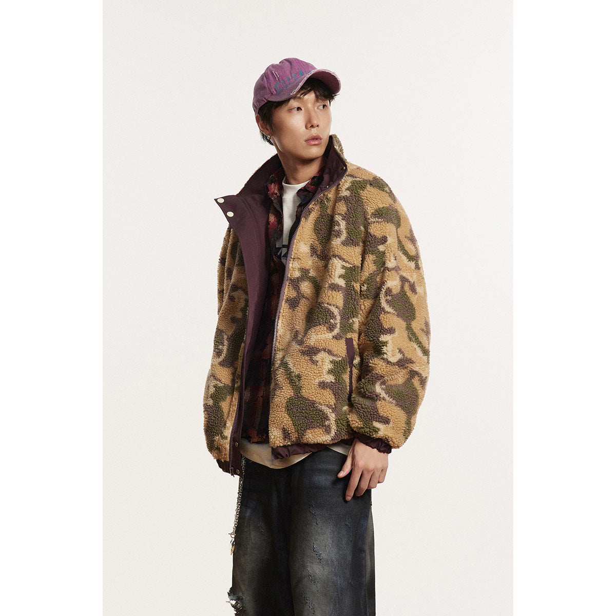 Three-quarter view of a model in a tan and olive camouflage fleece jacket with burgundy trim and dark trousers.