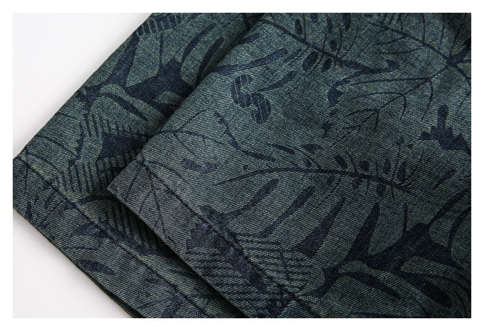 Close-up of folded blue-gray garment fabric with a dark abstract leaf and line print and visible stitching.