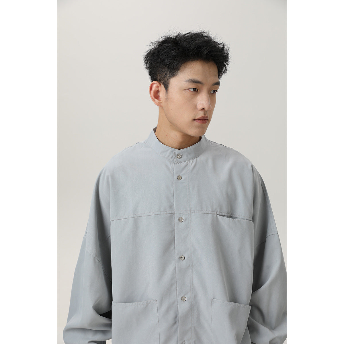 Close view of a model wearing a light gray stand-collar button shirt with a horizontal chest seam and two patch pockets.