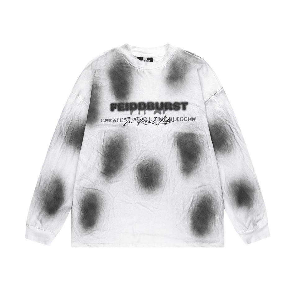 White long-sleeve crew-neck top with gray-black blurred spots and a chest wordmark print, flat lay front view