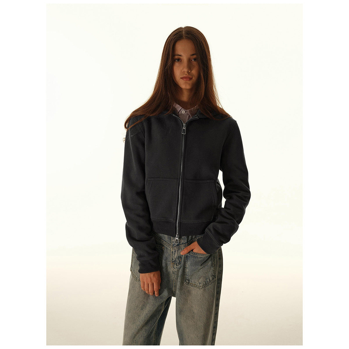 Front view of a model wearing a black zip-up hoodie with a hood, front pockets and ribbed cuffs, paired with jeans.