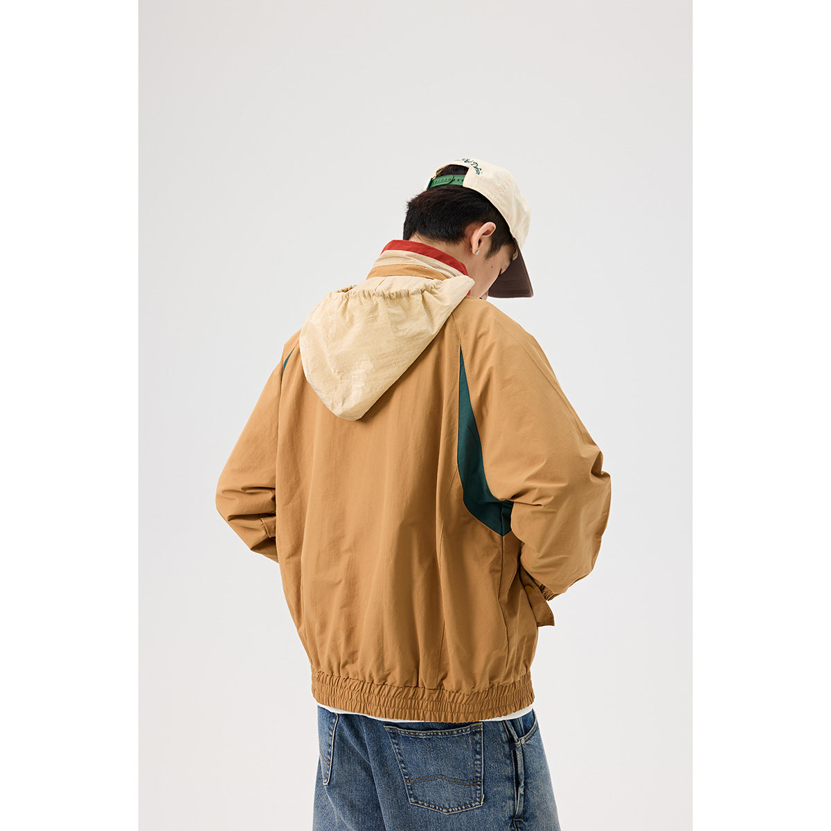 Back view of a model wearing a tan jacket with a pale hood, dark teal side panels and an elastic hem.