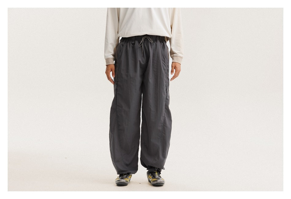 Model wearing loose charcoal-gray pants with an elastic drawstring waist and gathered ankles, shown from the front.