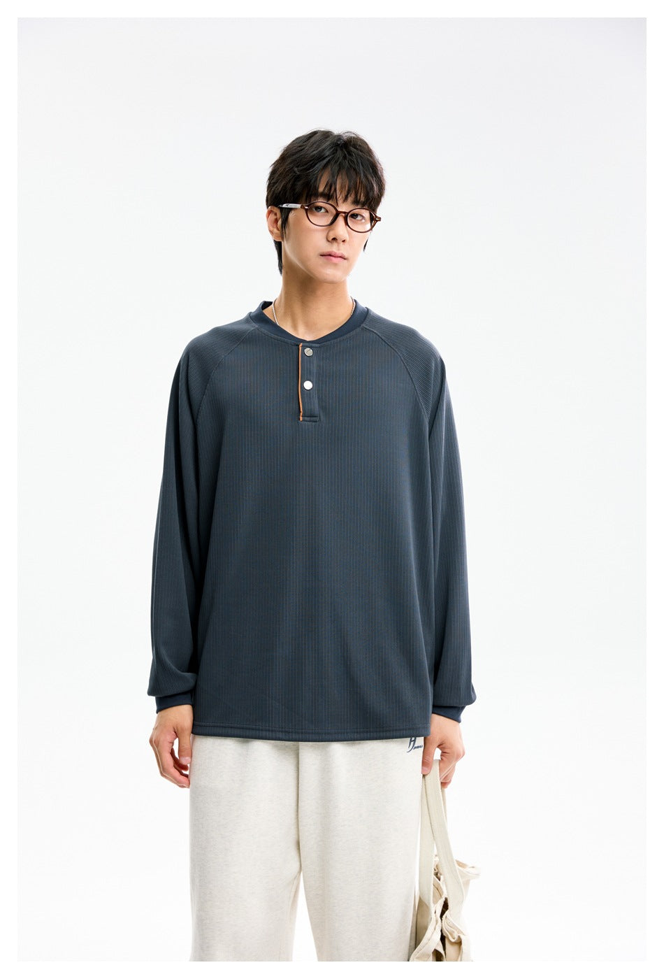 Front view of a model wearing a slate blue long-sleeve henley with a two-button placket and cream pants.