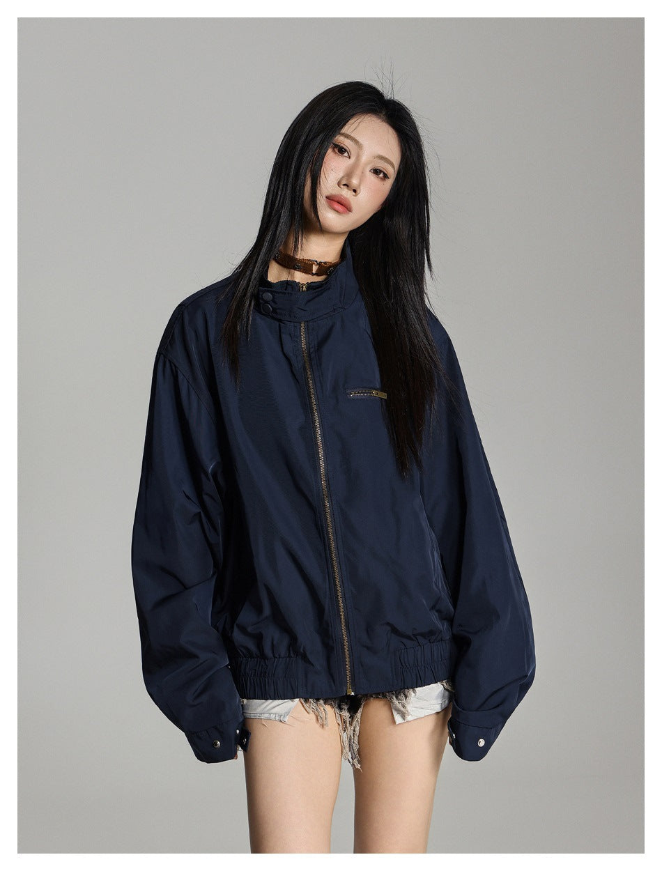 Model wearing a zipped navy jacket with a stand collar, chest zip pocket, and gathered hem.
