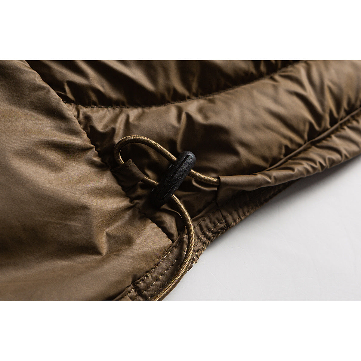 Close-up of a brown quilted jacket's hem drawcord and black toggle.