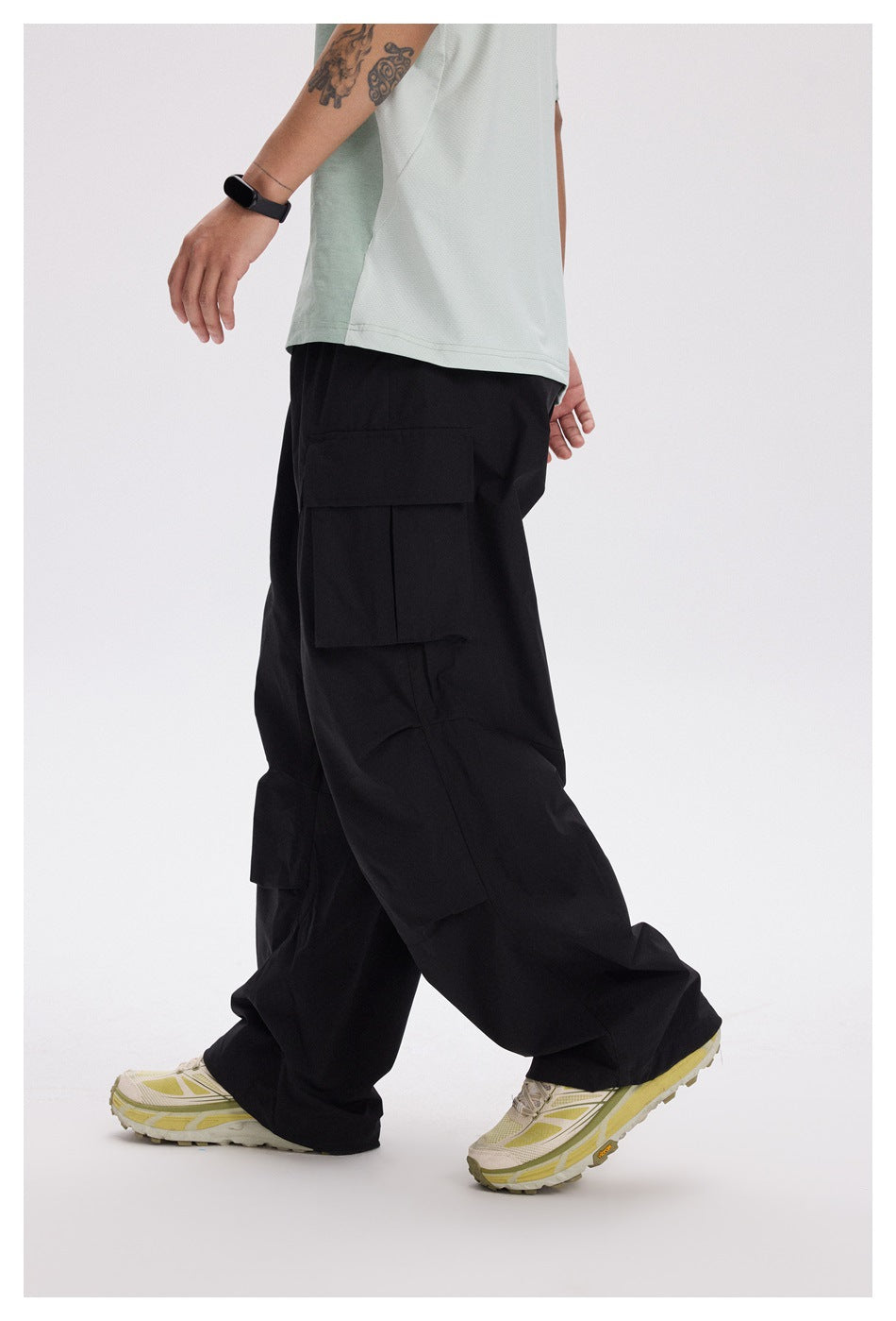 Side view of a model wearing loose black cargo pants with large flap pockets and a pale green shirt.