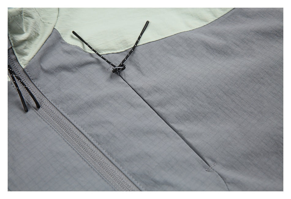 Close-up of the gray jacket front with a zip pocket, black cord pulls, and pale sage shoulder panel.