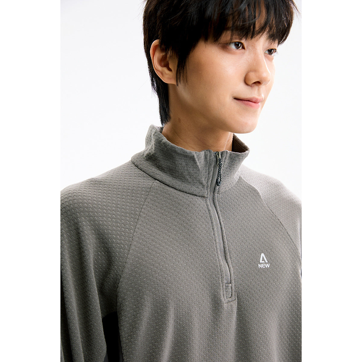 Close-up of a model wearing a textured gray quarter-zip pullover with a high collar and small chest logo.