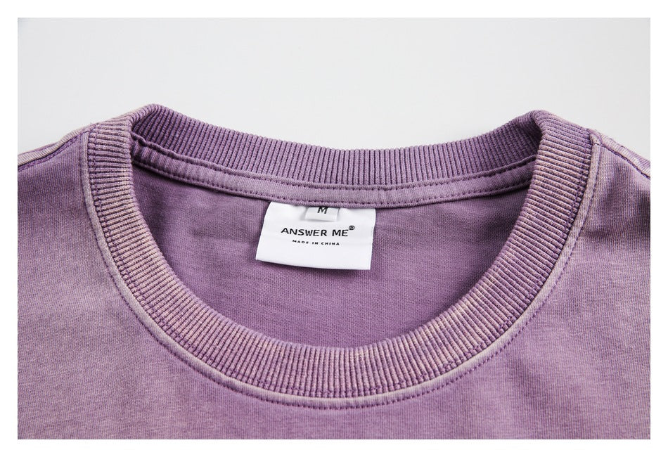 Close-up of a purple T-shirt's ribbed crew neck and sewn label reading “ANSWER ME” and “MADE IN CHINA.”