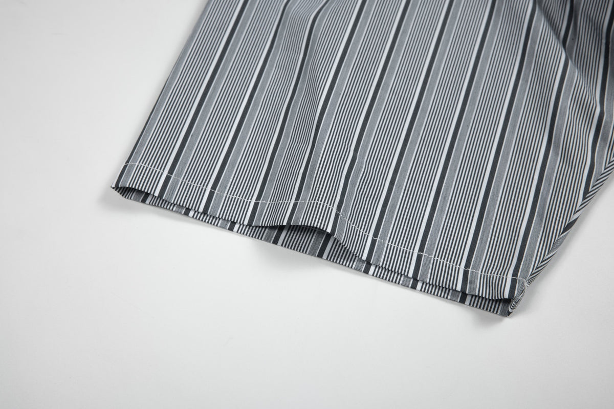 Close-up of the curved, stitched hem of a black, gray, and white vertically striped shirt.
