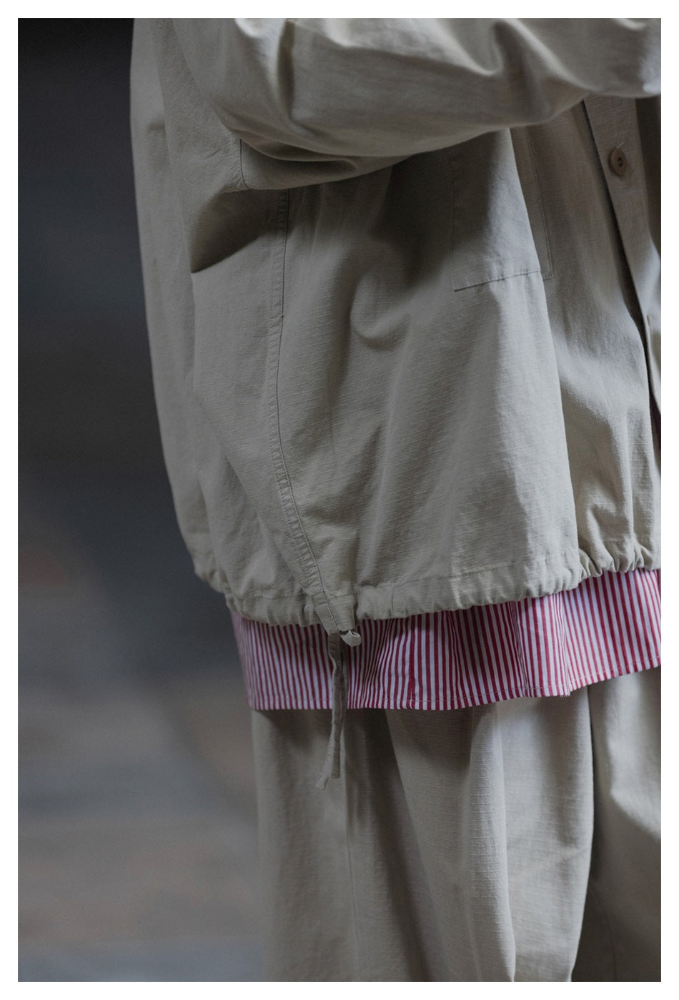 Close-up of the jacket's gathered hem and drawstring above a pink-and-white striped shirt.