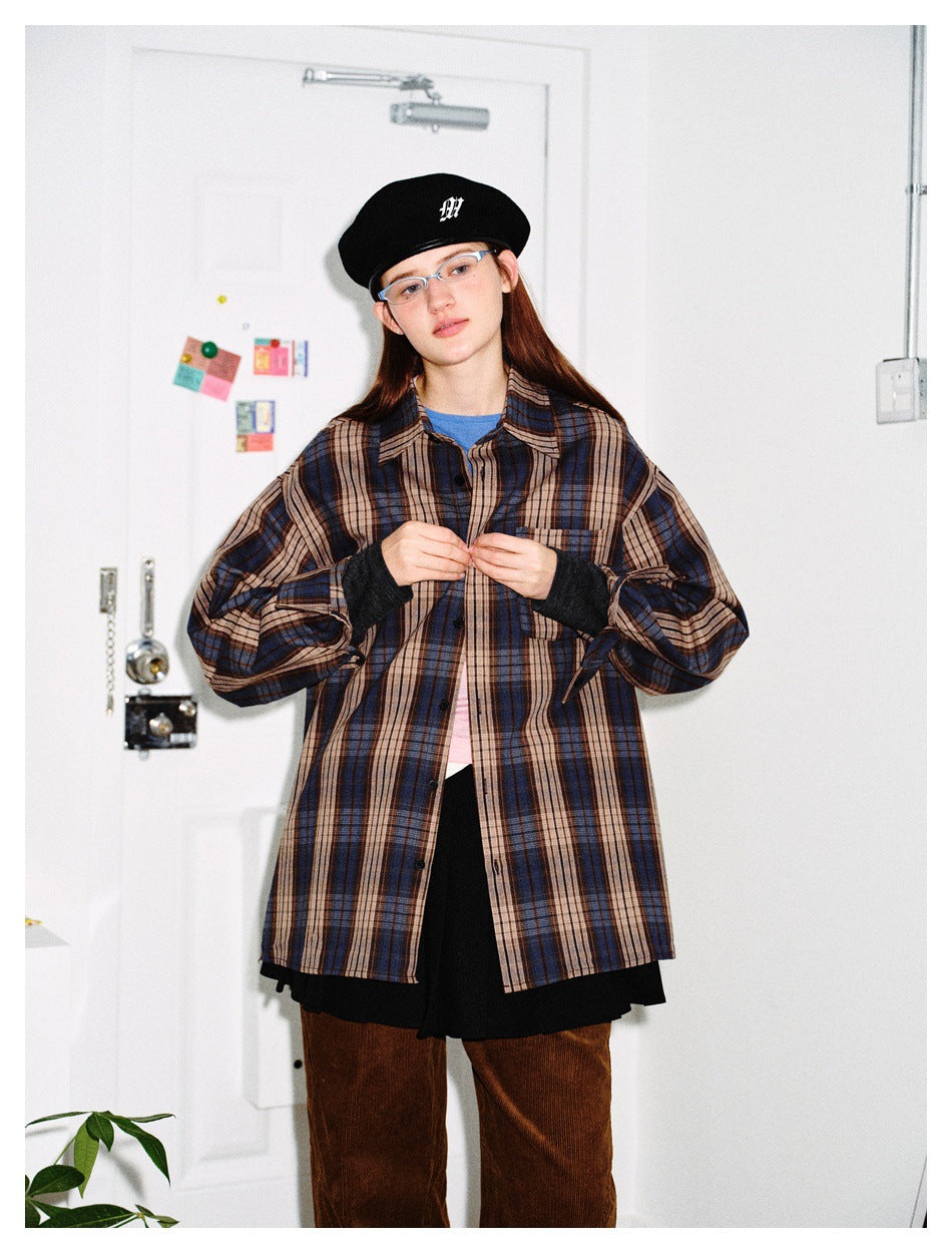 Model wearing oversized blue, brown and beige plaid button-up shirt open over a blue tee with black skirt and brown pants