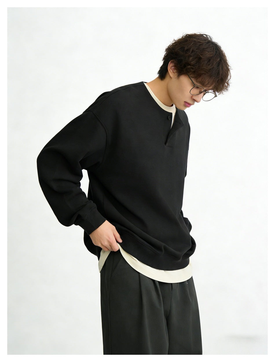Close view of a model wearing a black oversized button-placket sweatshirt over a cream shirt.
