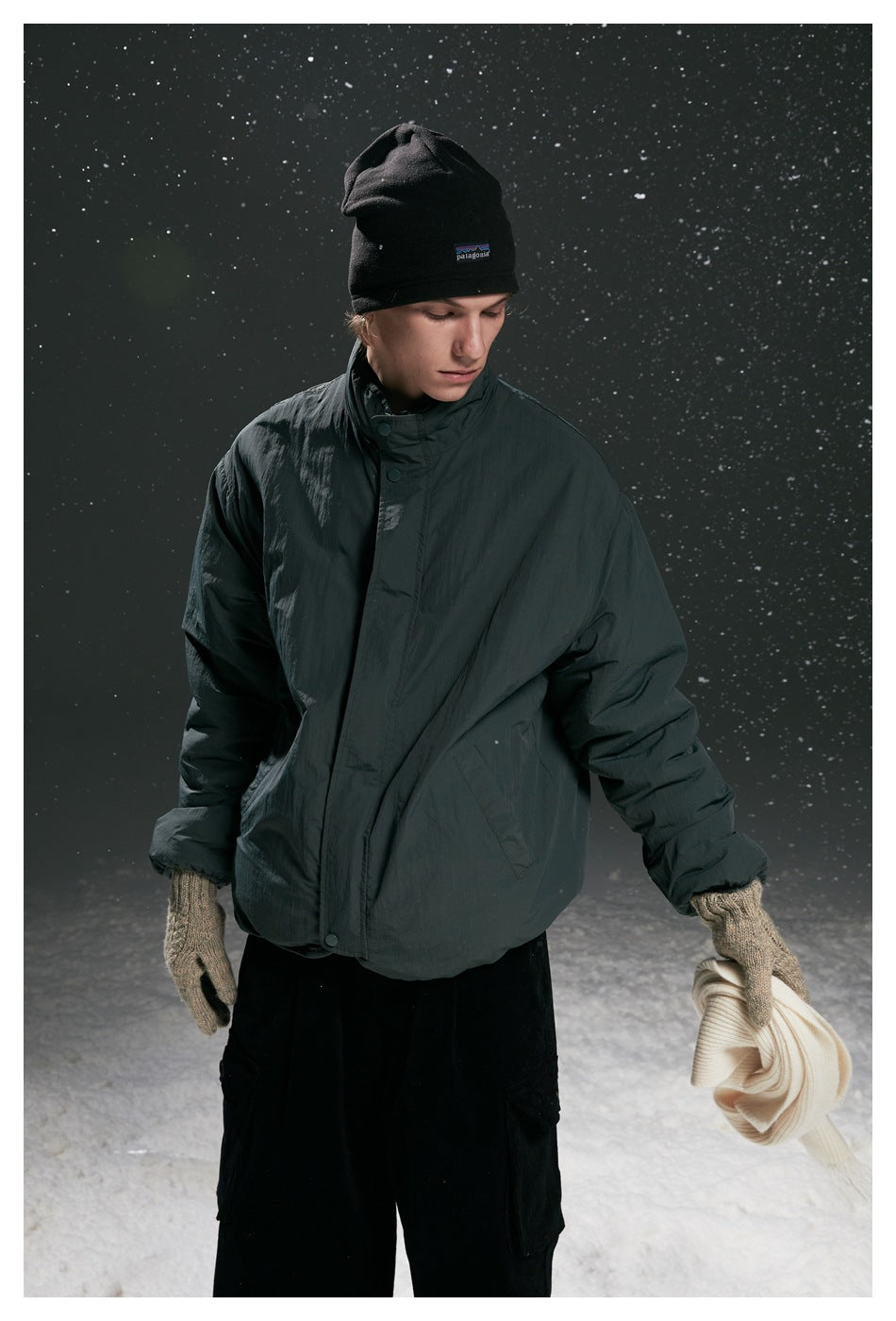 Close three-quarter view of model wearing the dark green stand-collar jacket with black cargo pants in a snowy scene